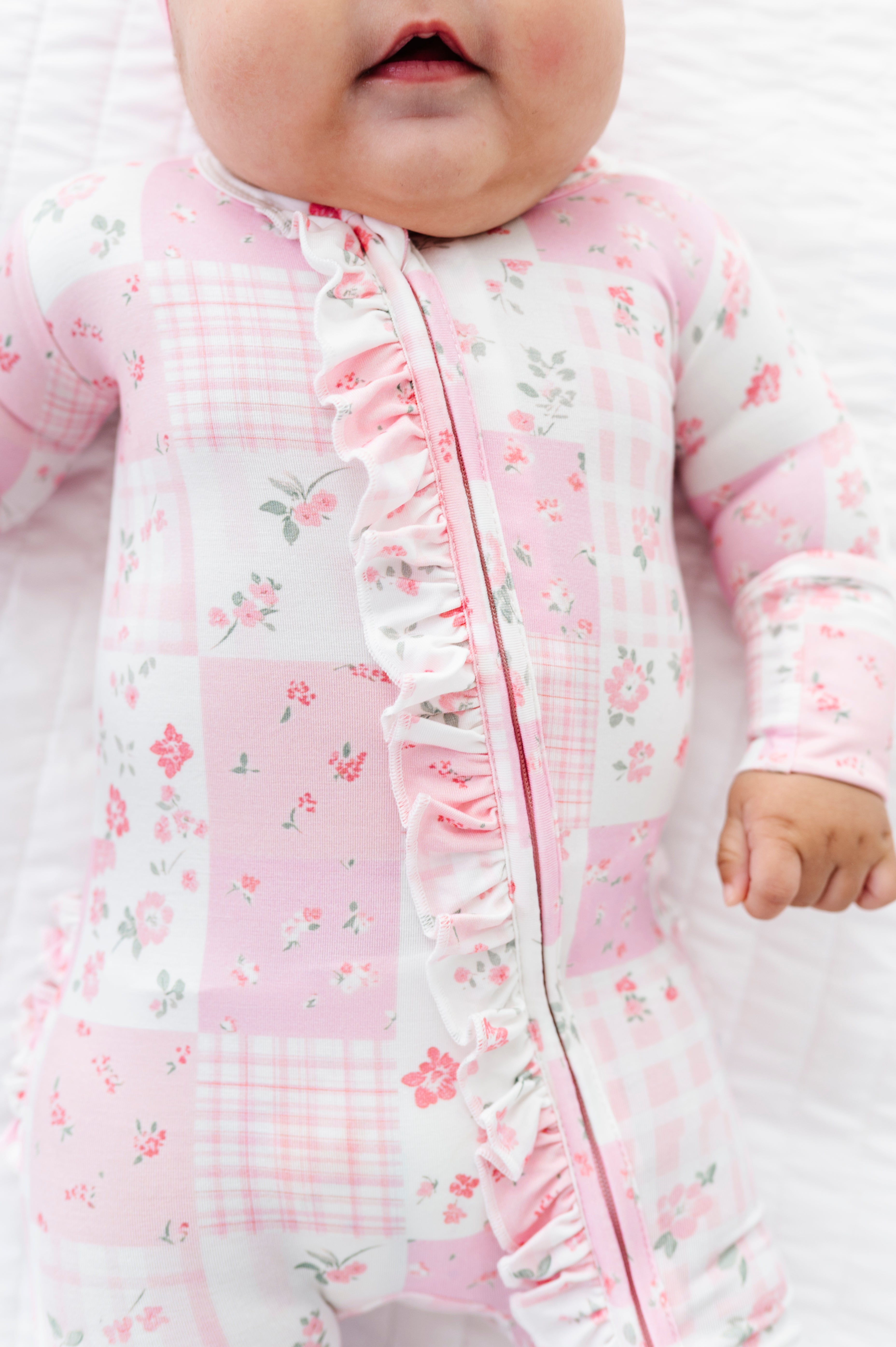 Baby in a pink floral and checkered bamboo zip romper outfit with ruffled details.